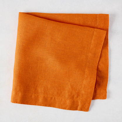 Persimmon HG Signature hand-dyed orange linen napkin, 22-inch square, folded on a white surface.
