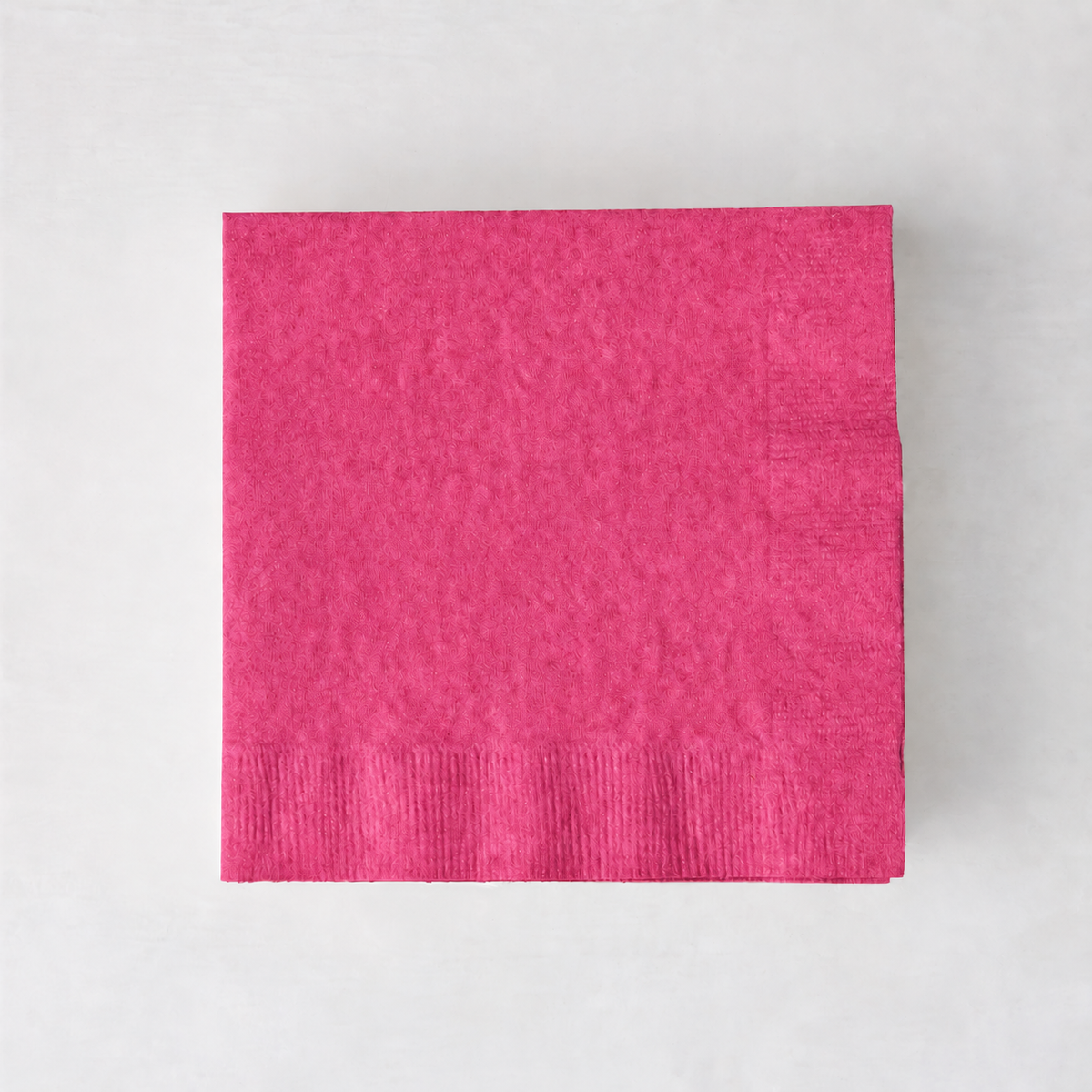 Square magenta pink 3-ply paper cocktail napkin on a light background.