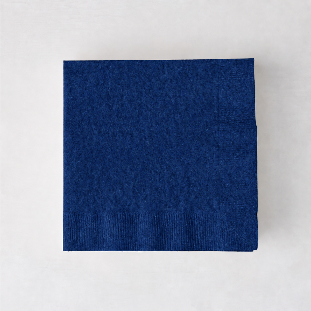 Square navy blue 3-ply paper cocktail napkin on a light background.