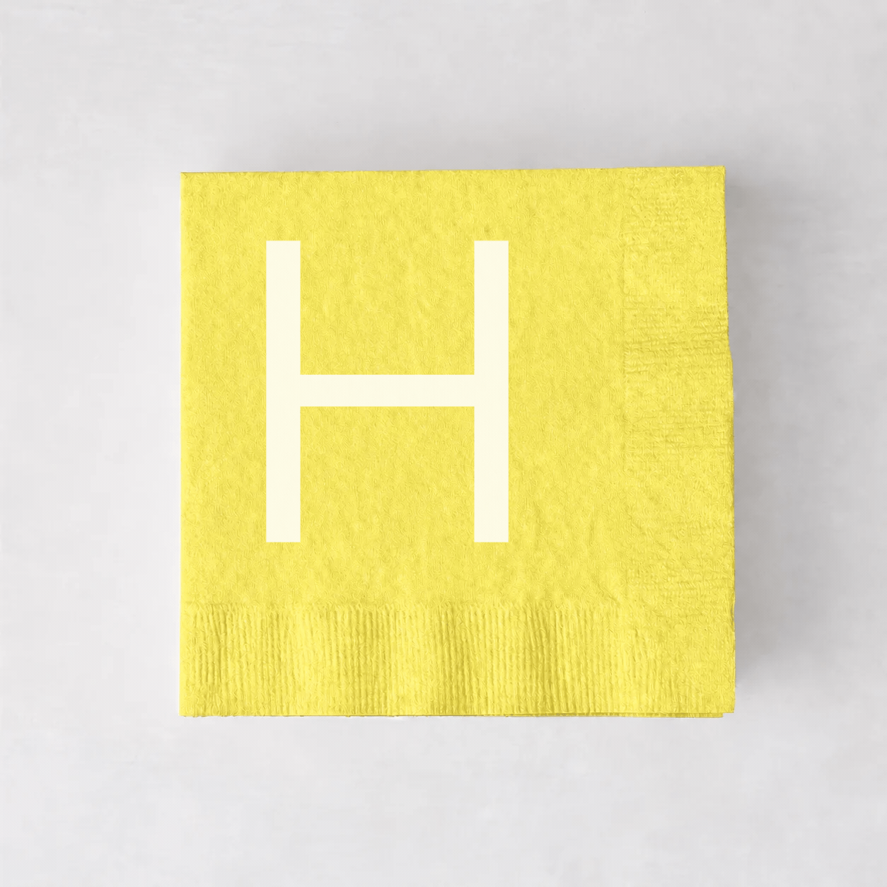 Personalized pale yellow 5.5-inch square paper cocktail napkin with a white letter H monogram.