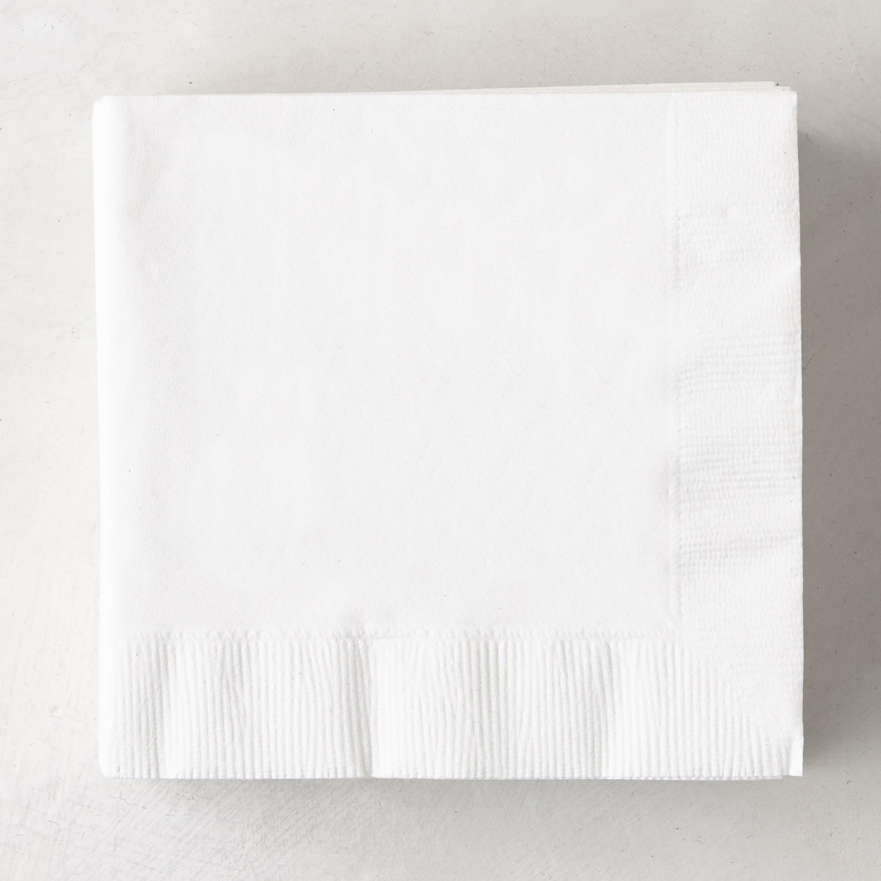 Stack of white, 3-ply disposable paper cocktail napkins, 5.5" square.