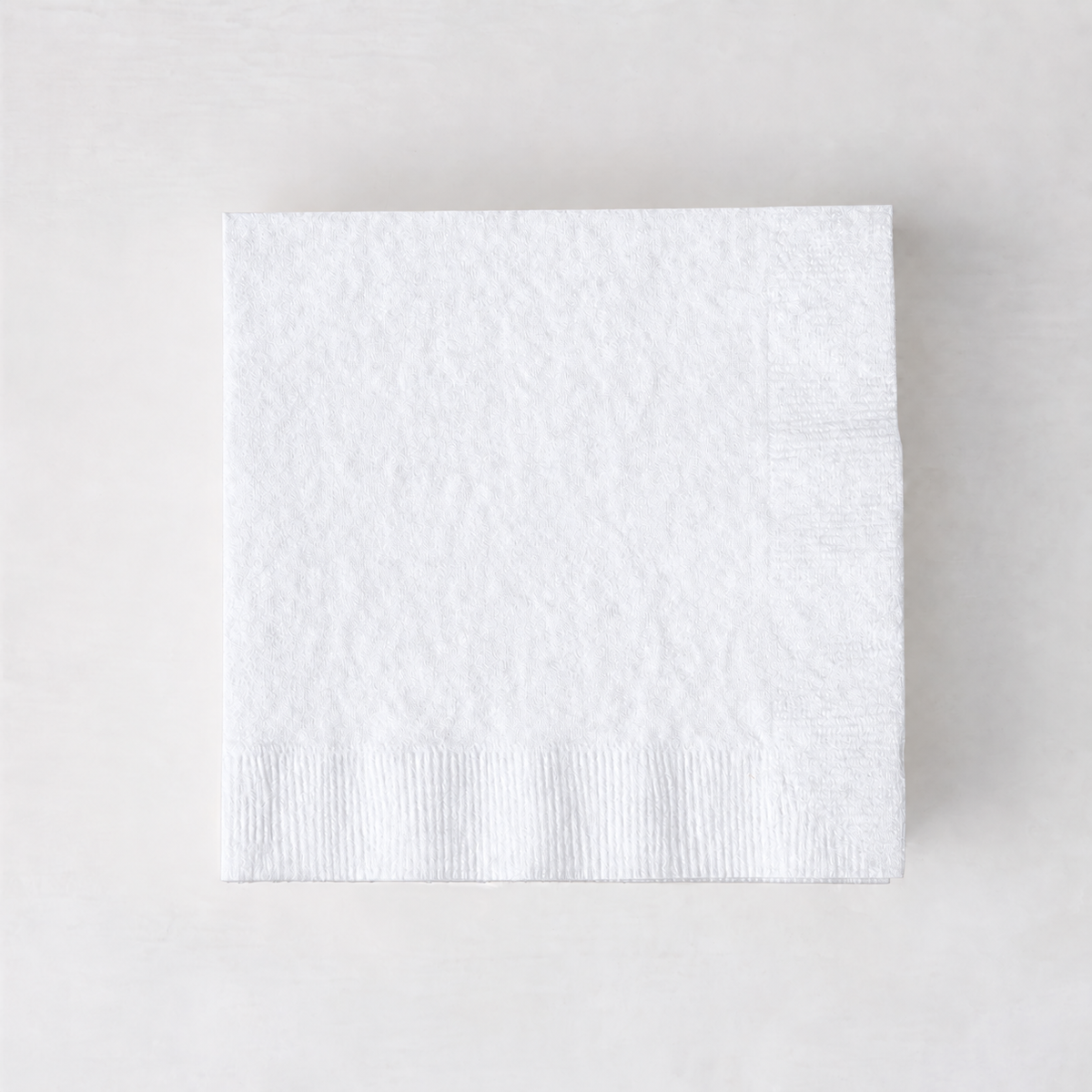 Square 5.5-inch white 3-ply paper cocktail napkin with a textured border on a light background.