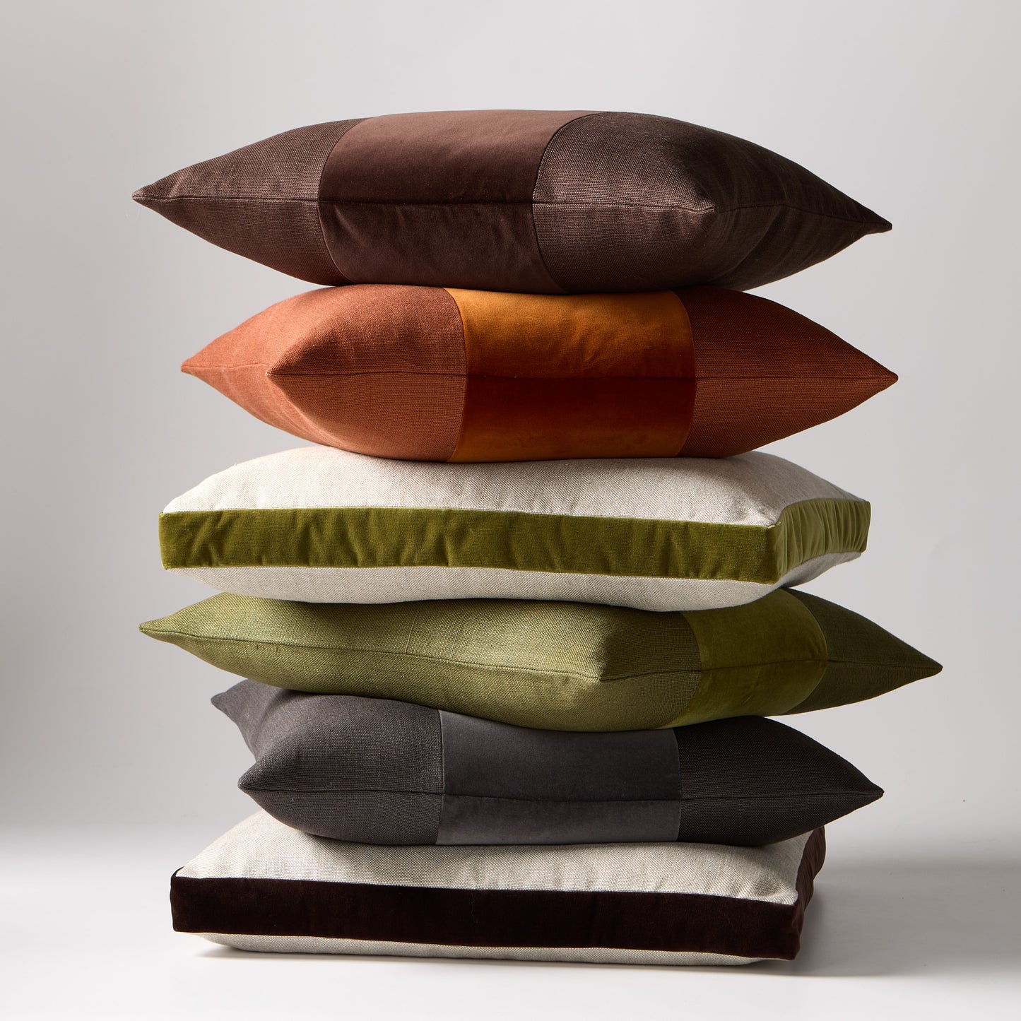 Stack of six 22" square linen and velvet pillows in brown, rust, green, and charcoal.