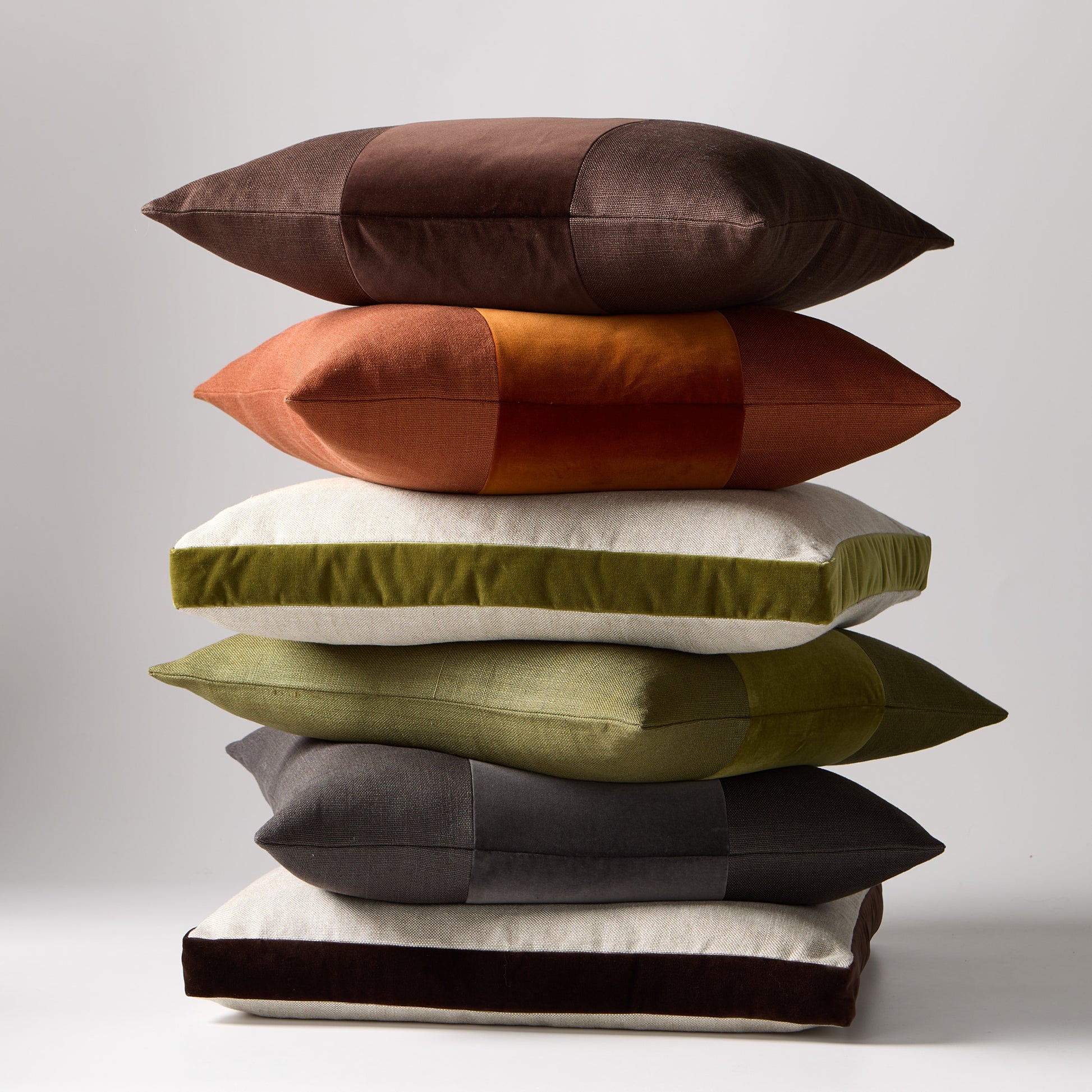 Stack of six 22" square linen and velvet pillows in brown, rust, green, and charcoal.