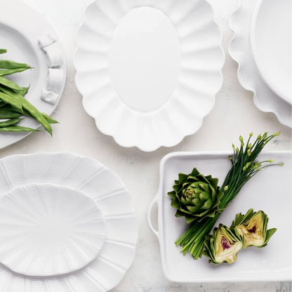 White Petal Large Oval Ceramic Serve Bowl with scalloped edges, surrounded by other white dinnerware and vegetables.