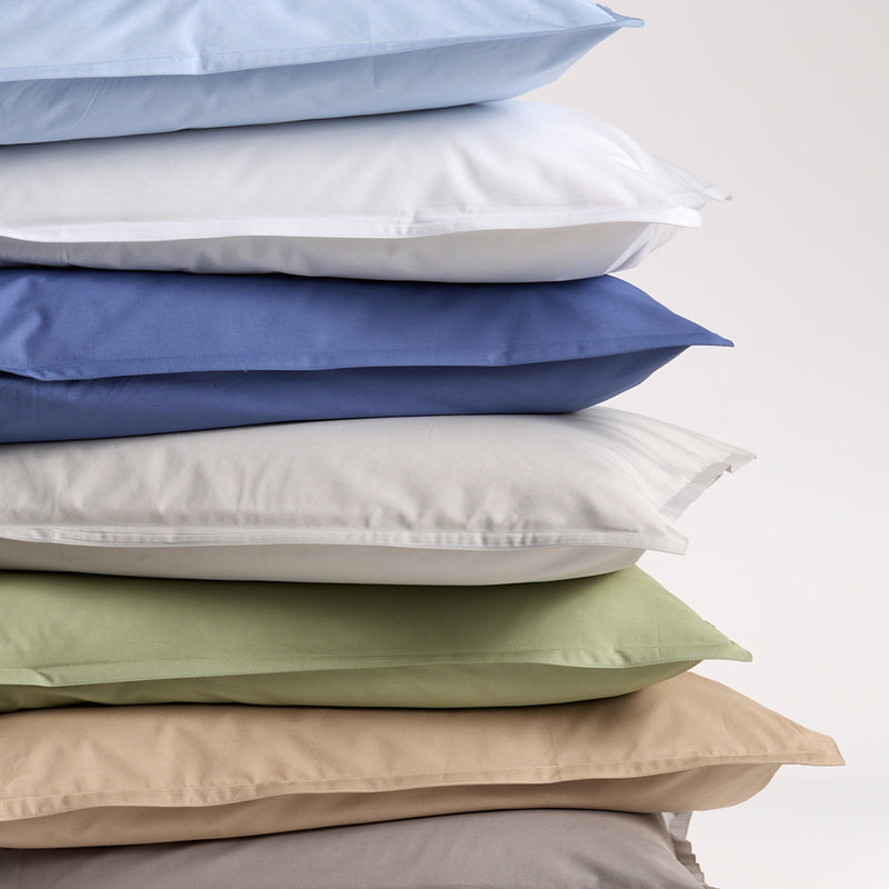 Stack of percale pillow shams in various colors: light blue, white, deep blue, off-white, sage green, and taupe.
