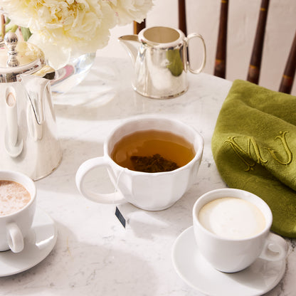 White Petal Stoneware Mug with tea, alongside other white mugs, silver creamer, and green napkin.
