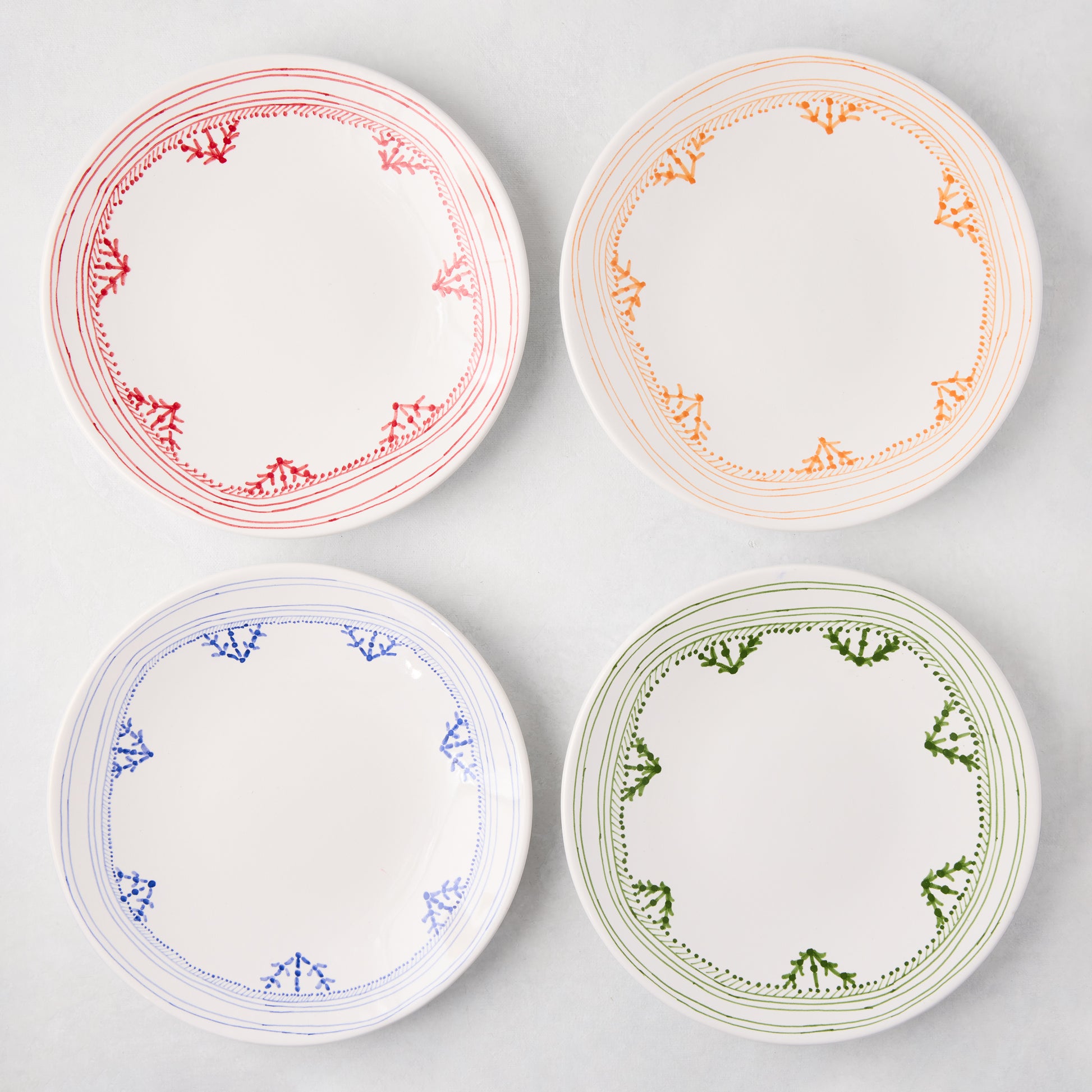 Four Peter Dunham + Hudson Grace Blue Fez hand-painted border salad plates in red, orange, blue, and green.