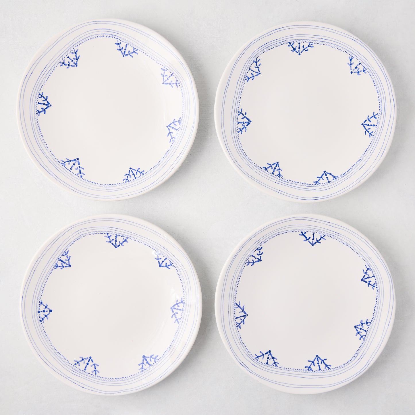 Four white Peter Dunham + Hudson Grace Blue Fez hand-painted border salad plates with blue patterns.