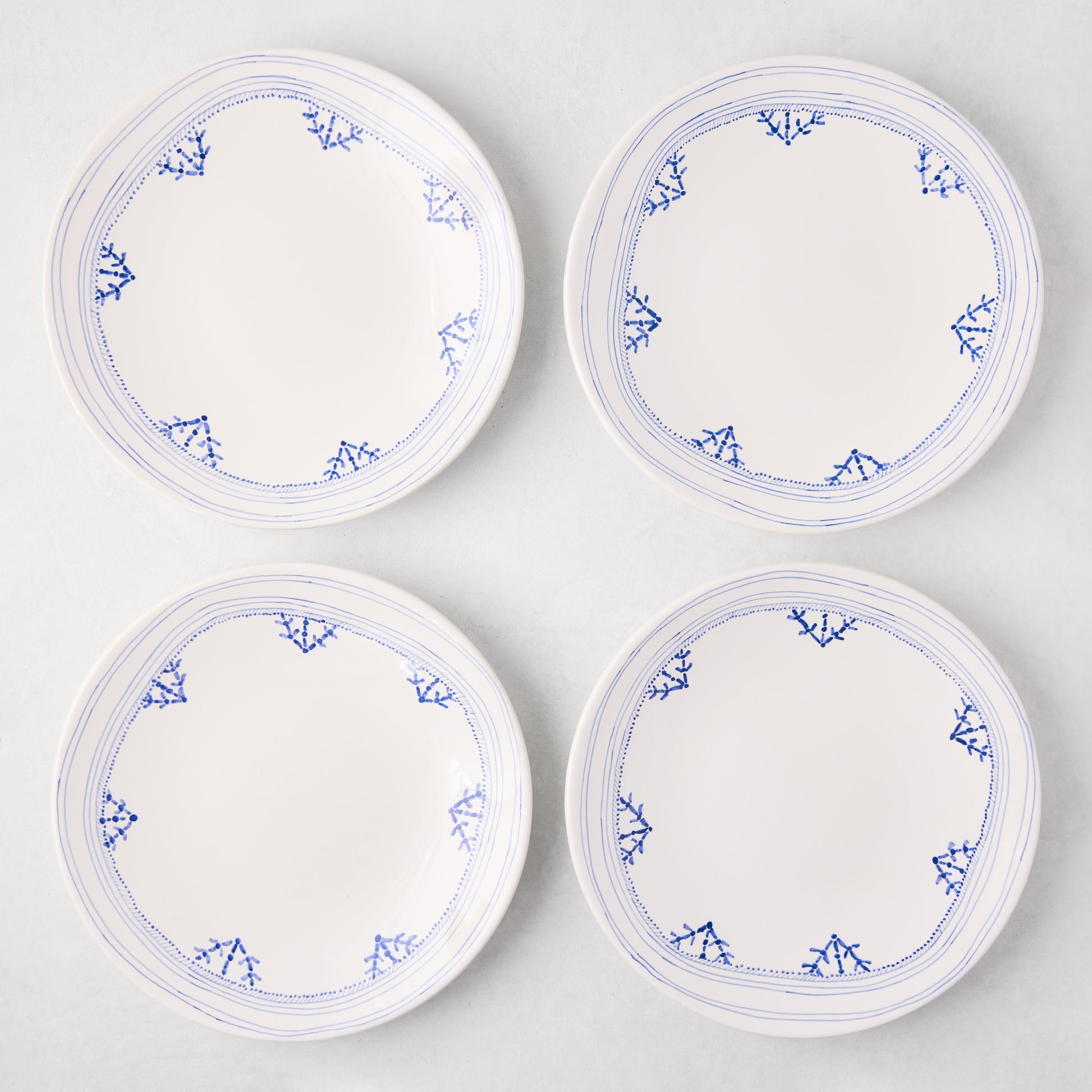 Four white Peter Dunham + Hudson Grace Blue Fez hand-painted border salad plates with blue patterns.