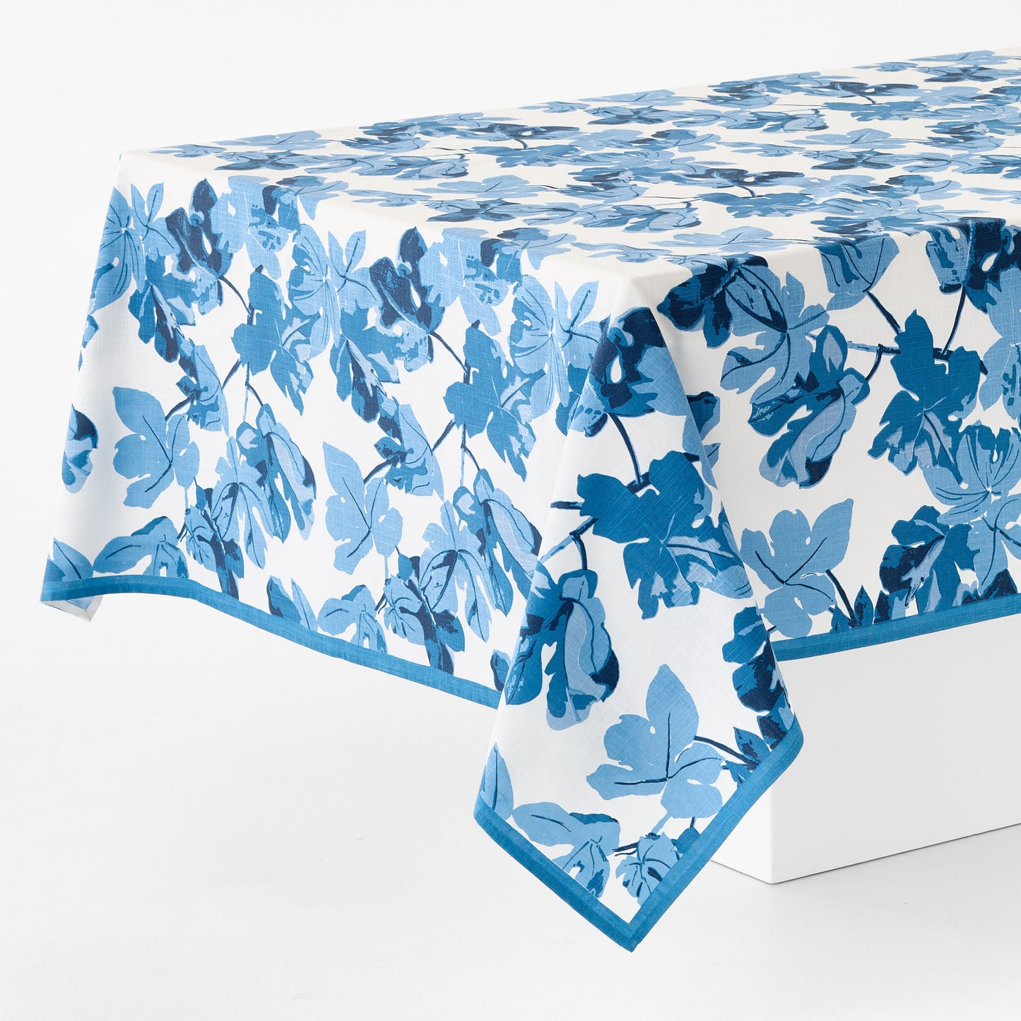 Peter Dunham blue fig leaf print cotton tablecloth with blue border on white background.