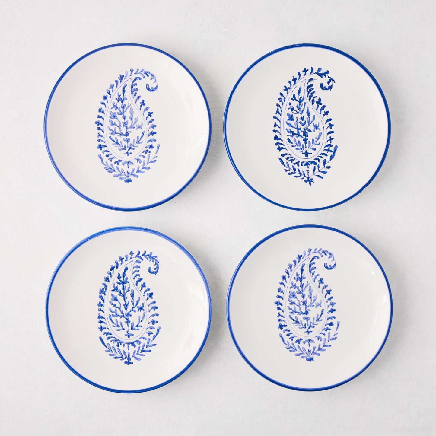 Four white Peter Dunham + Hudson Grace Blue Hand-Painted Kashmir Paisley Appetizer Plates with blue rims.