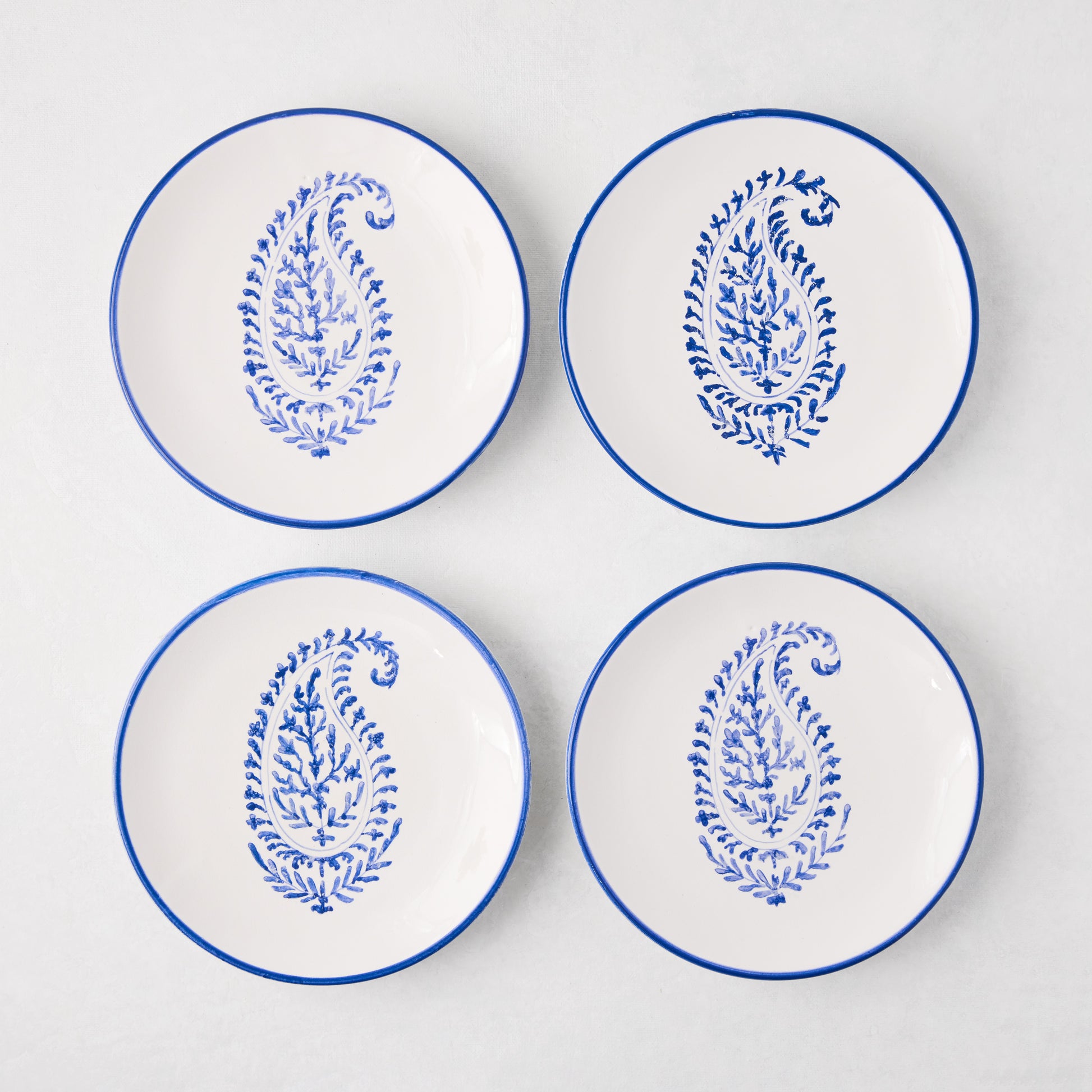 Four white Peter Dunham + Hudson Grace Blue Hand-Painted Kashmir Paisley Appetizer Plates with blue rims.