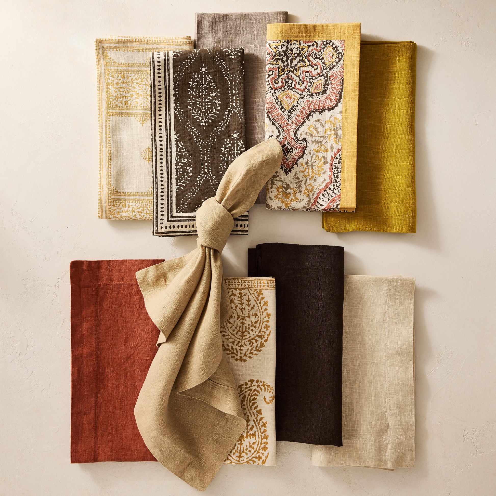 Peter Dunham + Hudson Grace Gold and Spice Orange Deeg printed cotton napkin with yellow border, surrounded by other patterned and solid napkins.