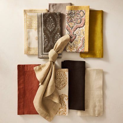 Peter Dunham + Hudson Grace Gold and Spice Orange Deeg printed cotton napkin with yellow border, surrounded by other patterned and solid napkins.