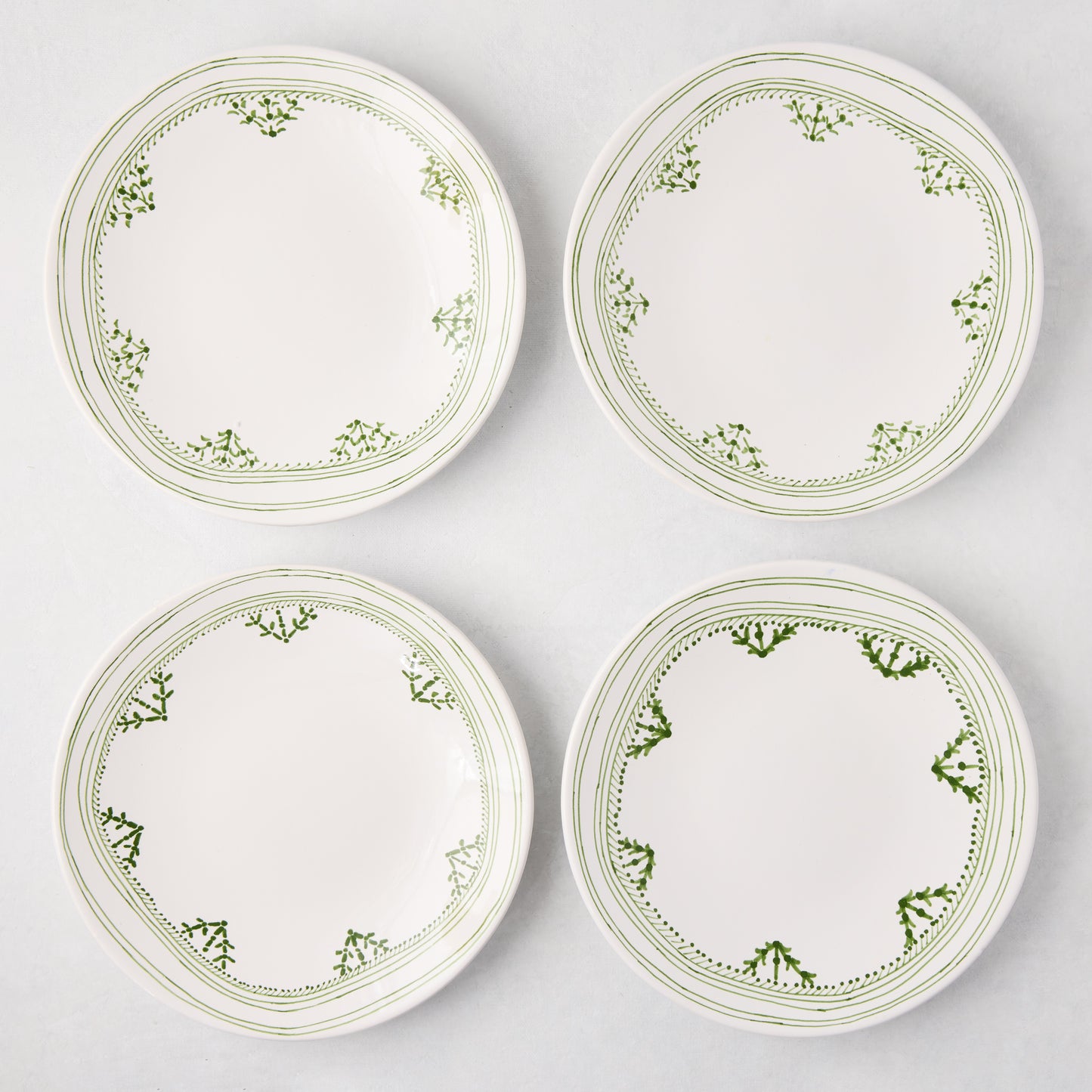 Four white Peter Dunham + Hudson Grace Green Fez hand-painted border salad plates with green patterns.