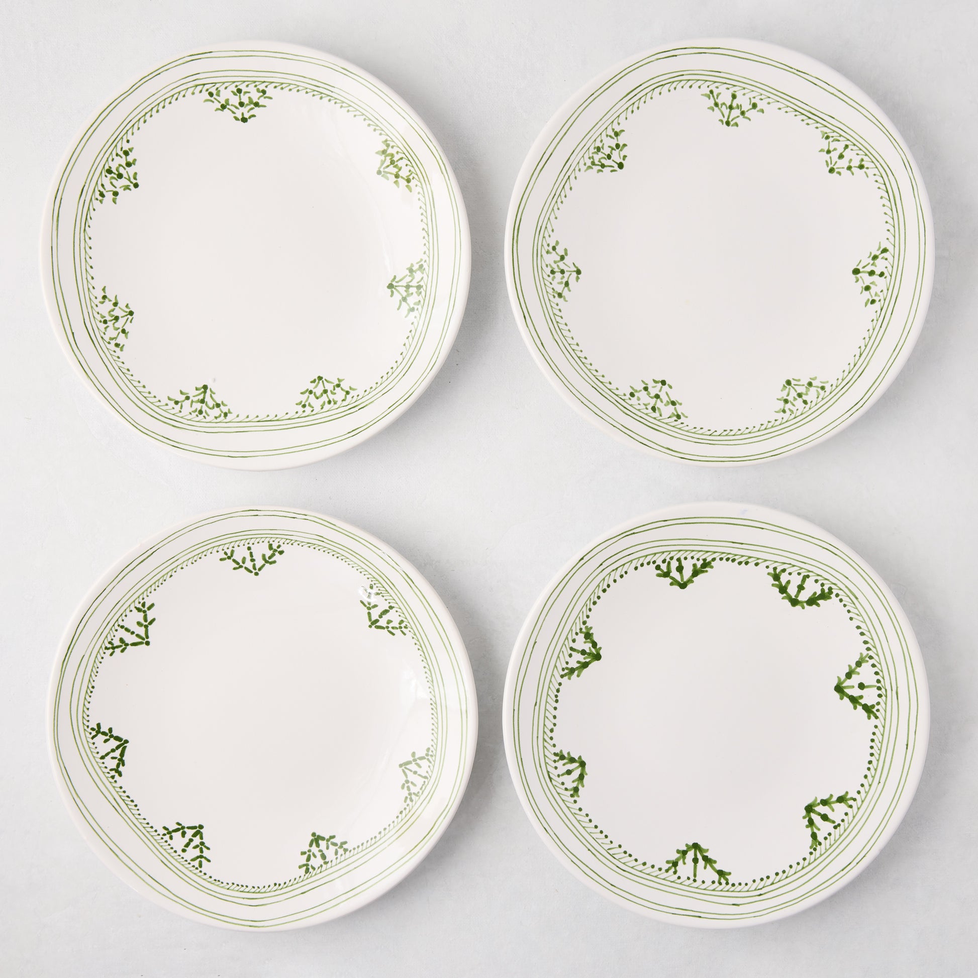 Four white Peter Dunham + Hudson Grace Green Fez hand-painted border salad plates with green patterns.