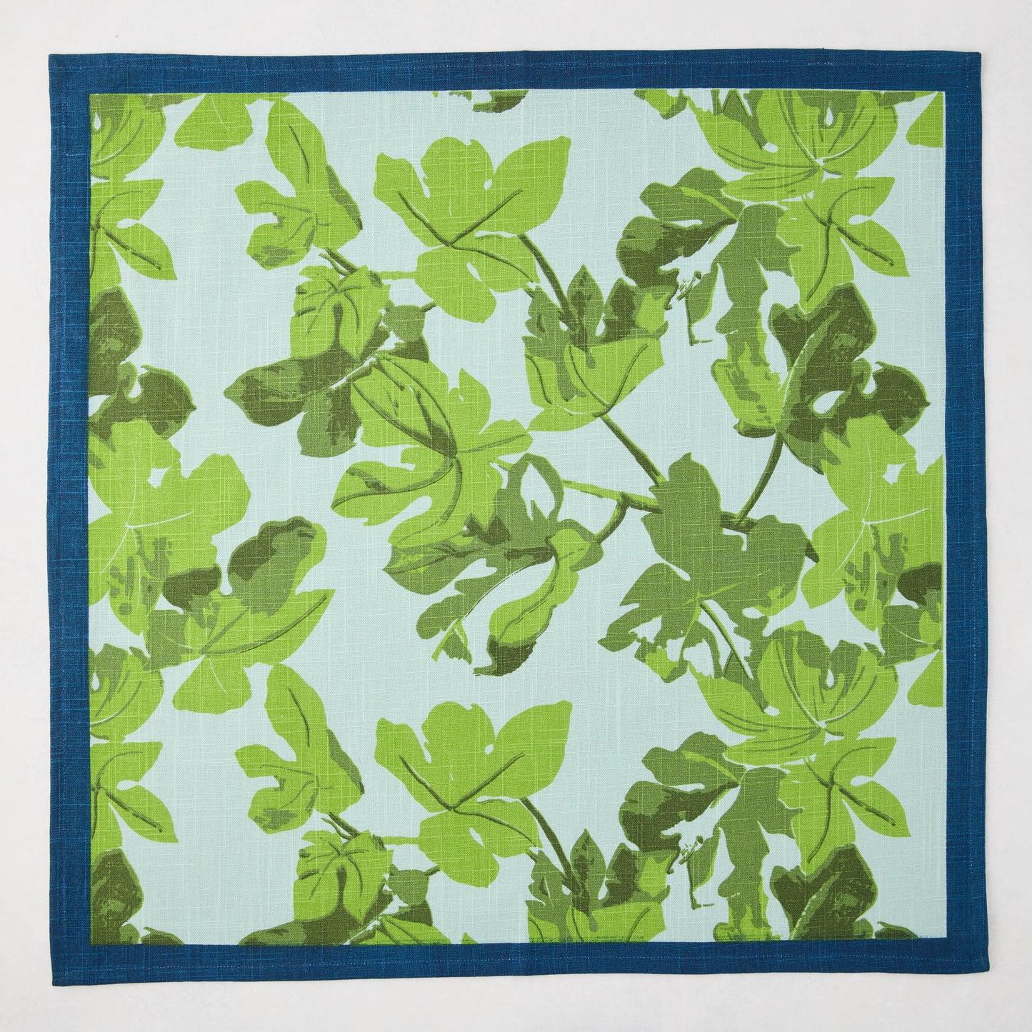 Peter Dunham + Hudson Grace green fig leaf printed blue cotton slub napkin with a dark blue border.