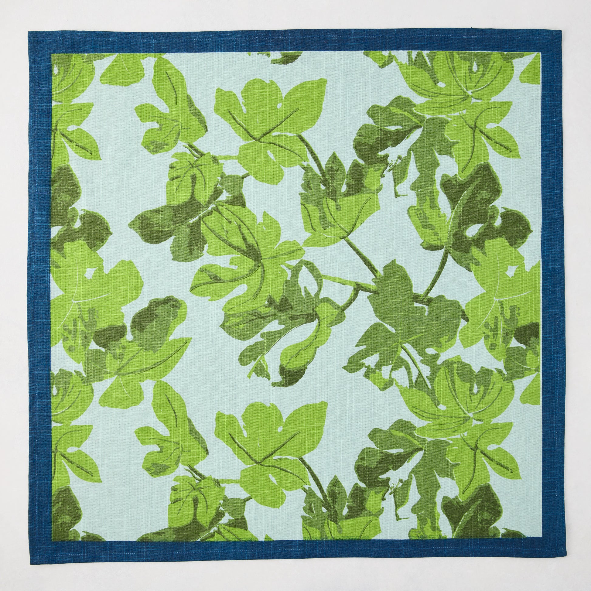 Peter Dunham + Hudson Grace green fig leaf printed blue cotton slub napkin with a dark blue border.