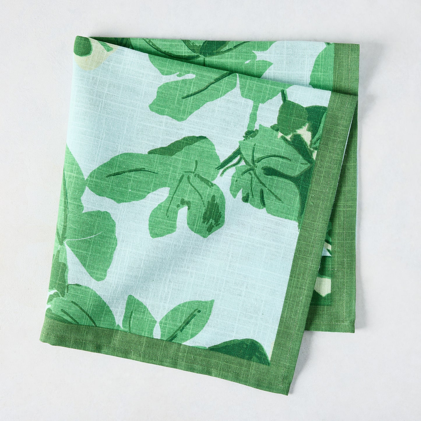Pale blue cotton slub napkin with bold green fig leaf print and a solid green border.