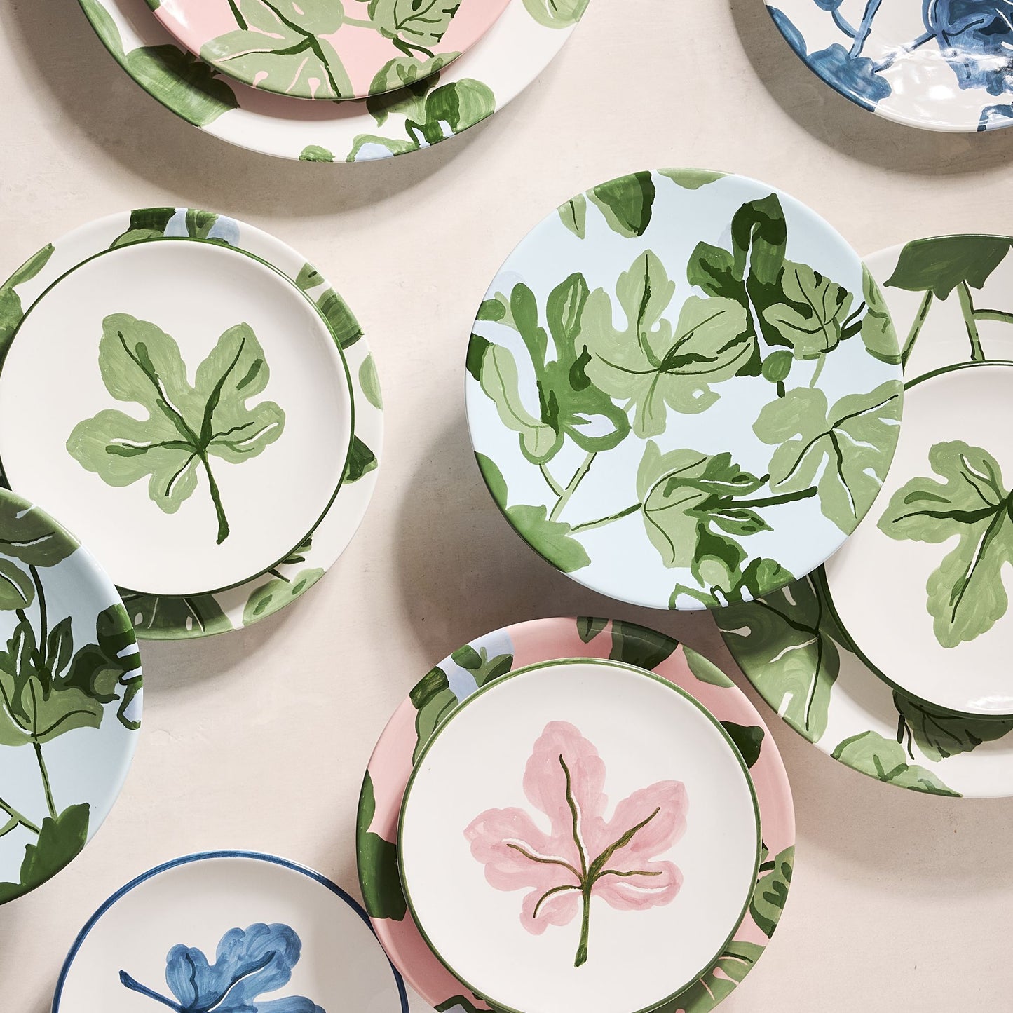 Hand-painted ceramic salad plates with green fig leaf patterns on blue, pink, and white backgrounds.