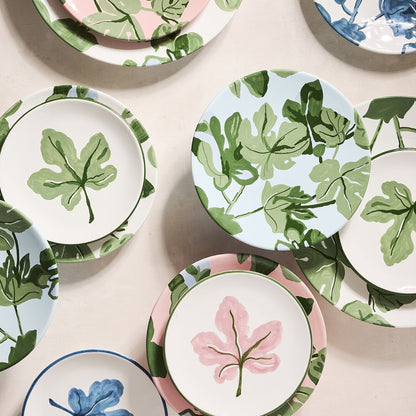 Hand-painted ceramic salad plates with green fig leaf patterns on blue, pink, and white backgrounds.
