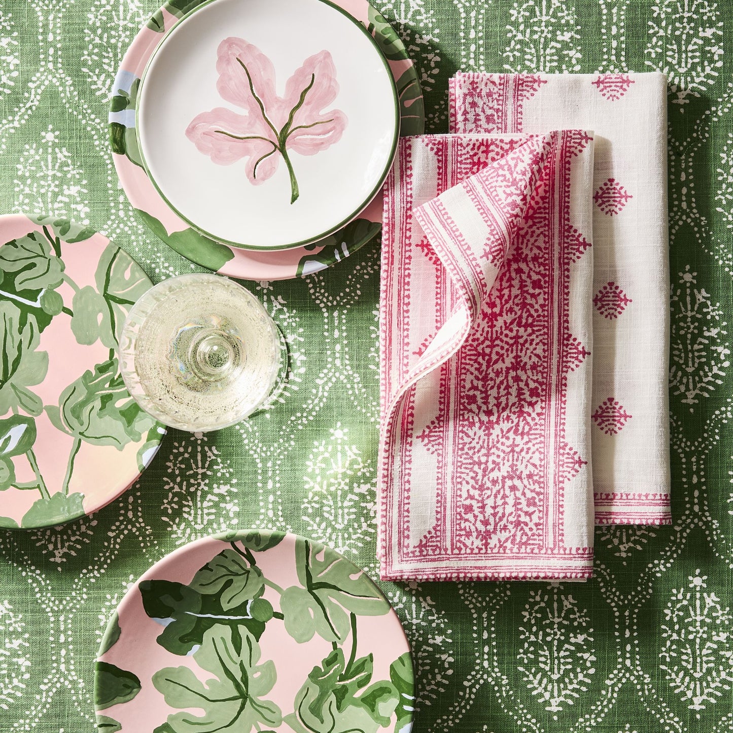 Hand-painted pink fig leaf appetizer plates with green borders on a patterned green tablecloth with pink napkins.