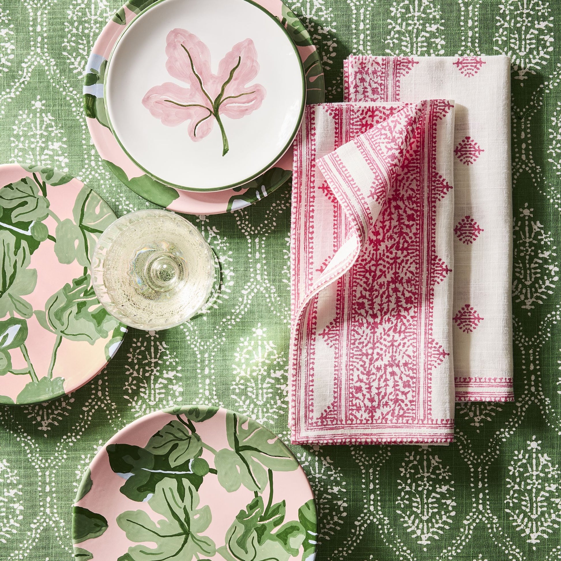 Hand-painted pink fig leaf appetizer plates with green borders on a patterned green tablecloth with pink napkins.