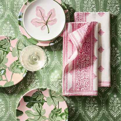 Hand-painted pink fig leaf appetizer plates with green borders on a patterned green tablecloth with pink napkins.