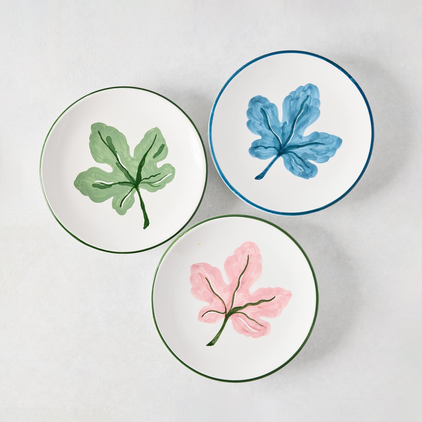 Three hand-painted appetizer plates: pink, green, and blue fig leaf designs with colored borders.
