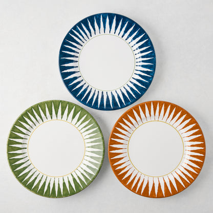 Three Peter Dunham + Hudson Grace hand-painted sunburst dinner plates: olive green, blue, and orange.