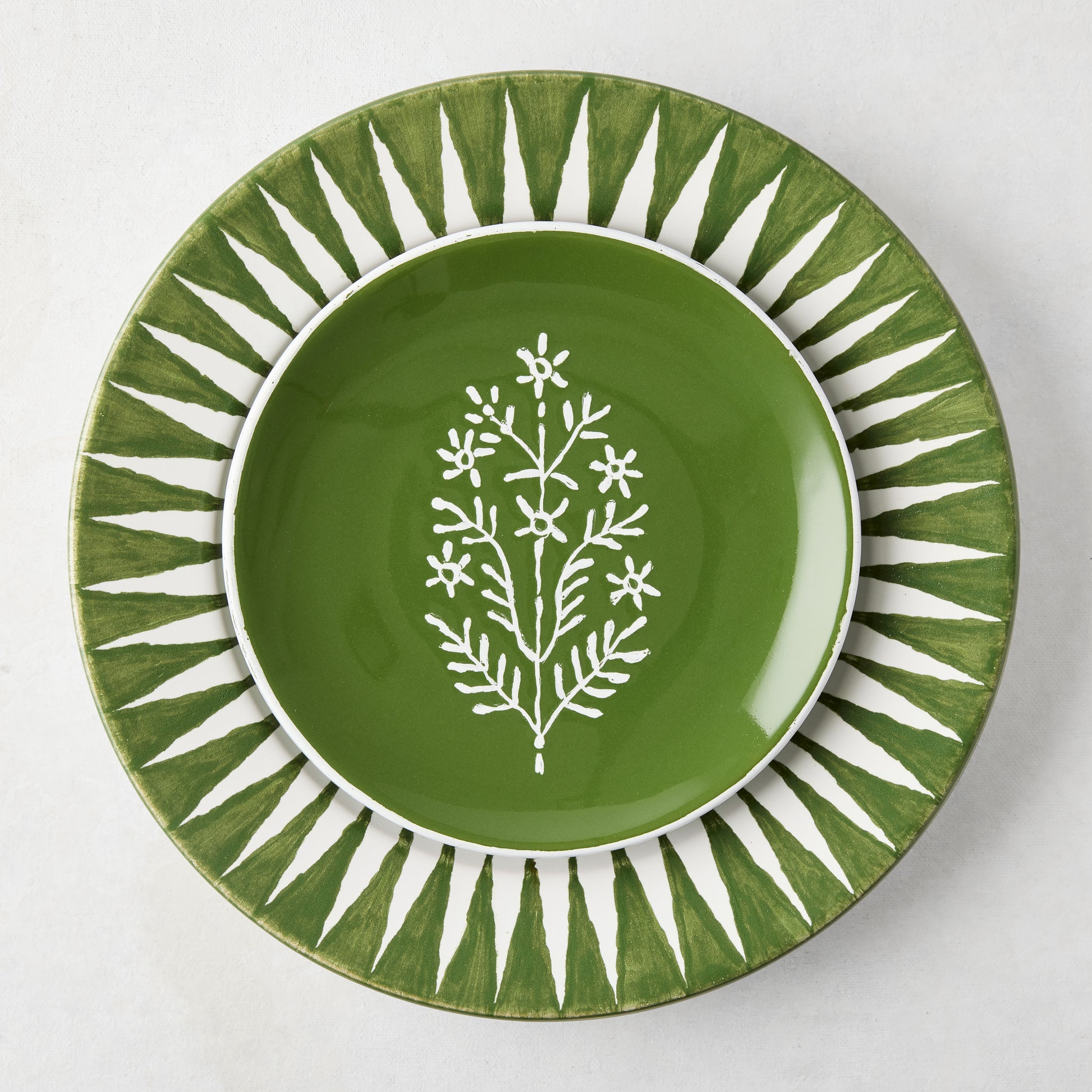 Peter Dunham + Hudson Grace Olive Green Hand-Painted Sunburst Dinner Plate with a smaller green plate featuring a white floral design.