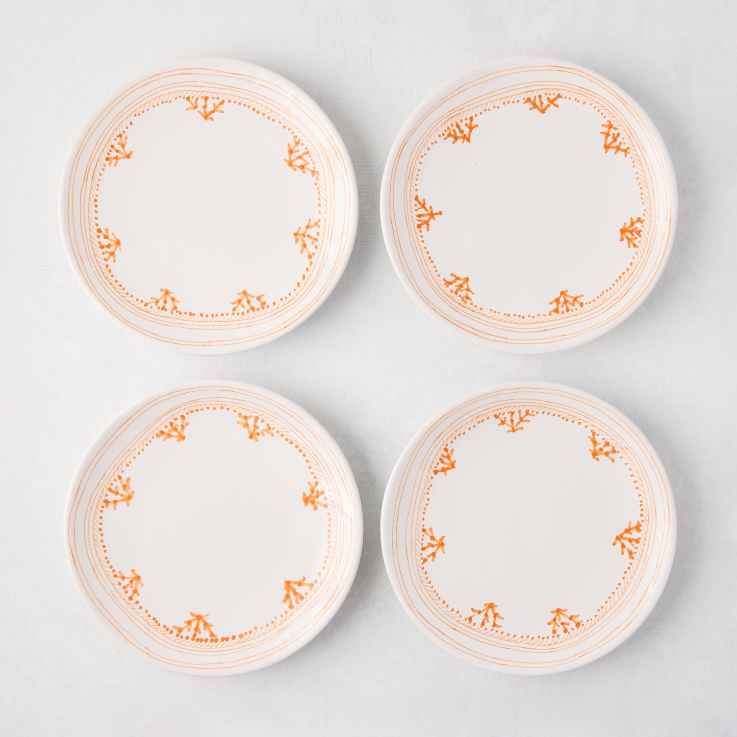 Four white Peter Dunham + Hudson Grace Orange Fez appetizer plates with hand-painted coral borders.