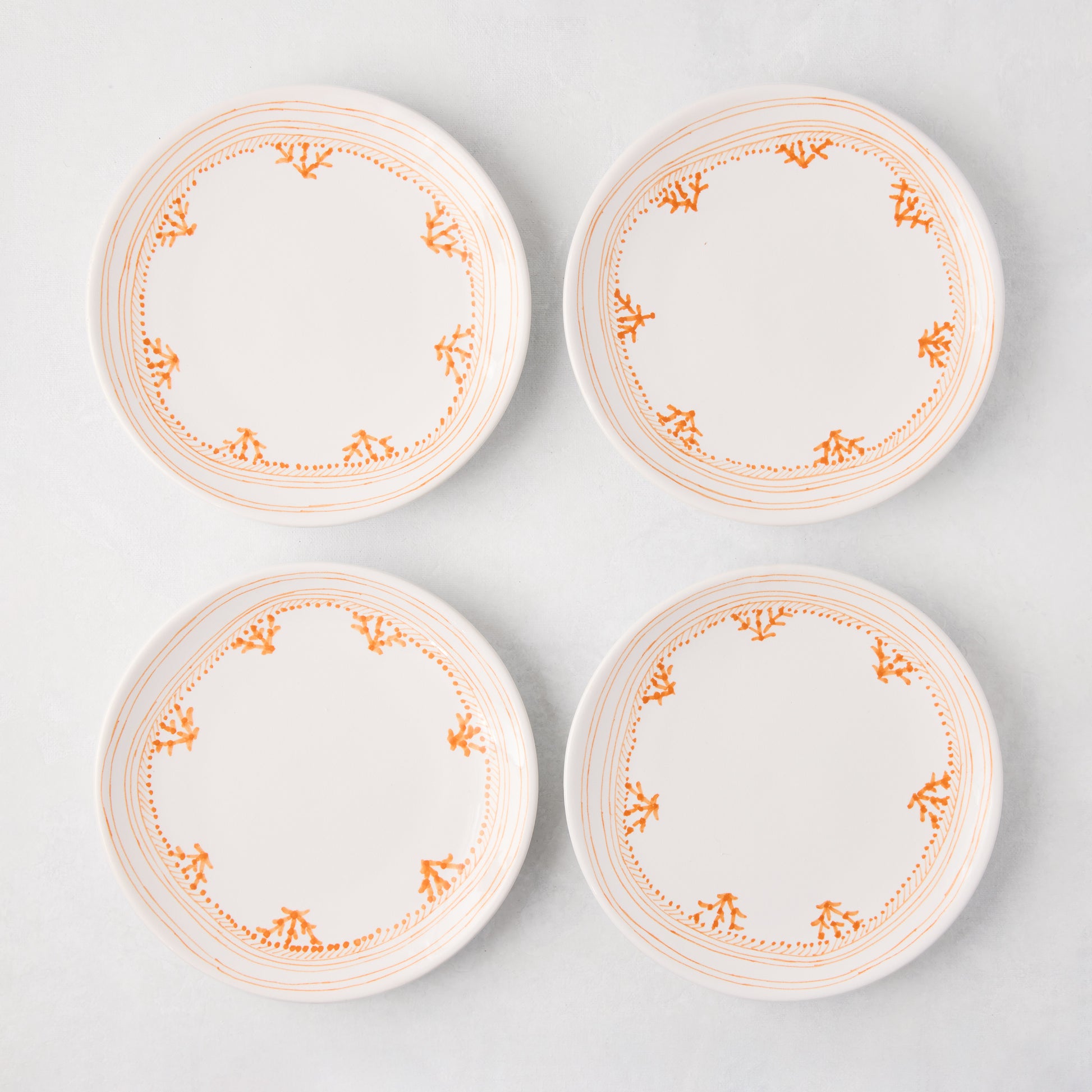 Four white Peter Dunham + Hudson Grace Orange Fez appetizer plates with hand-painted coral borders.