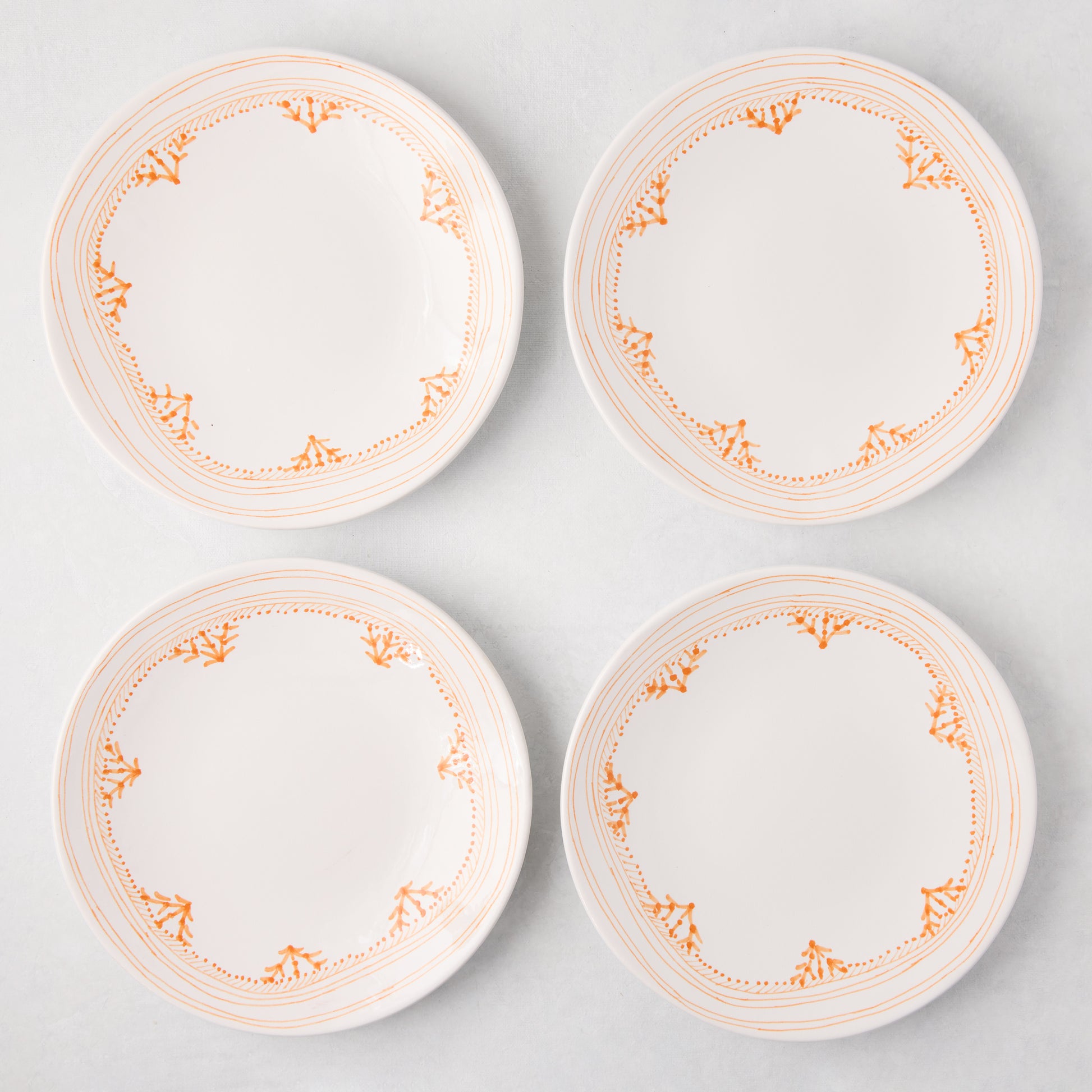 Four white Peter Dunham + Hudson Grace Orange Fez hand-painted salad plates with an orange border pattern.