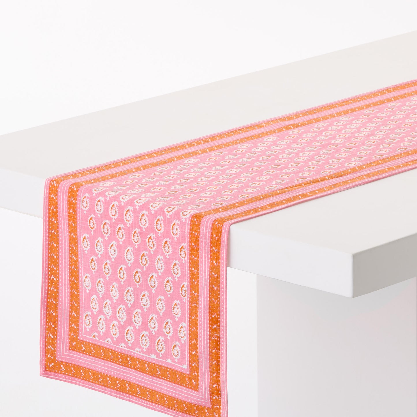 Pink and orange cotton slub table runner with a paisley print and graphic border, 108 by 18 inches.
