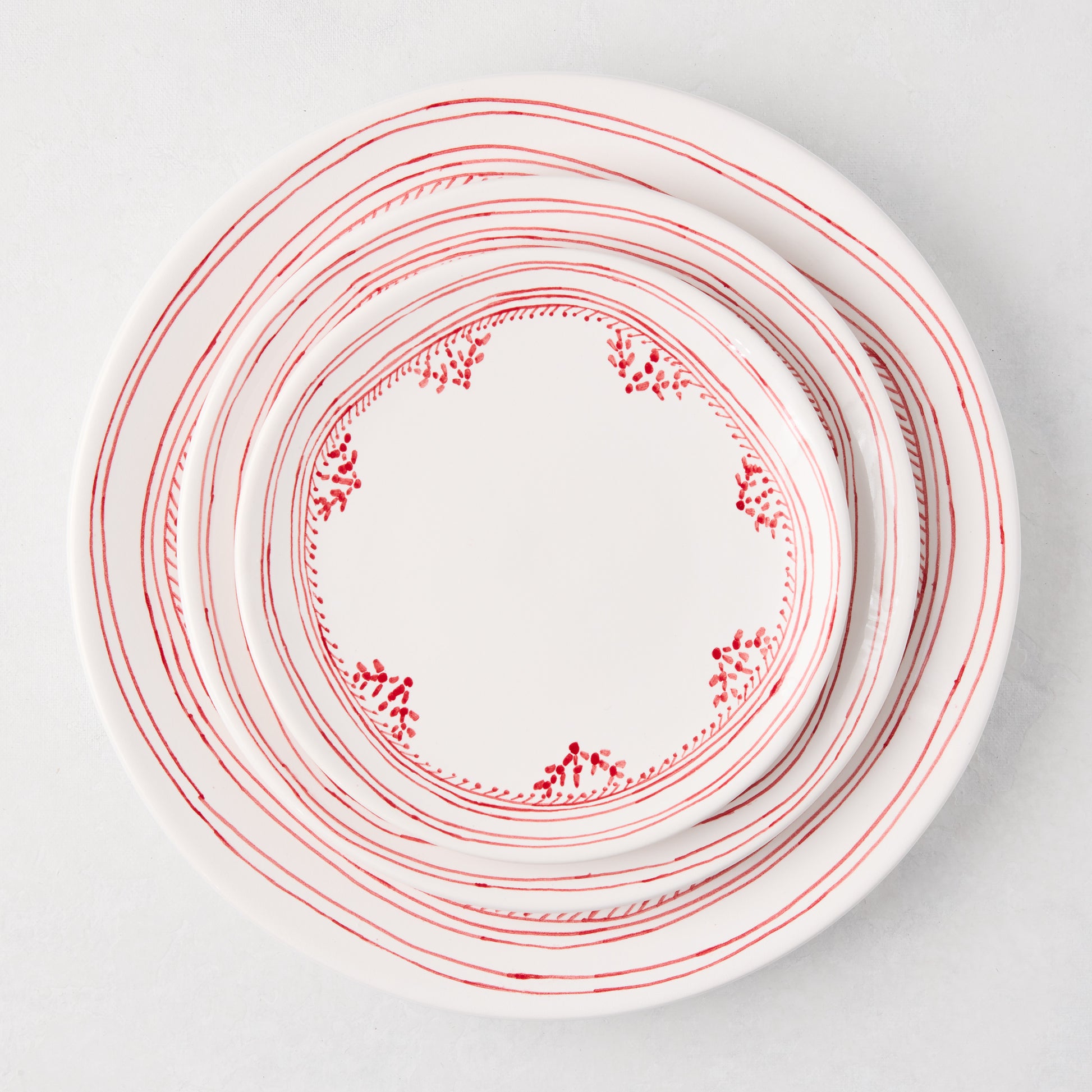 White ceramic appetizer plates with hand-painted red striped and dotted borders, stacked.