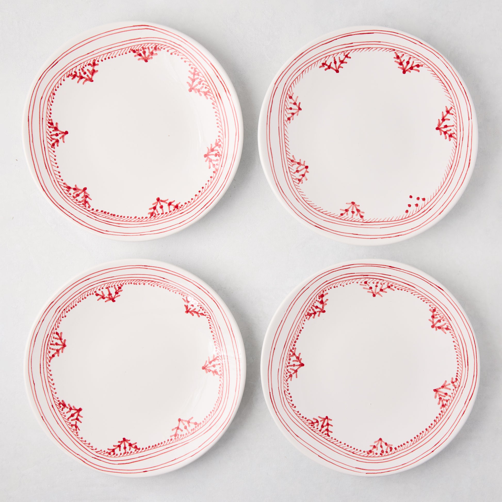 Four white Peter Dunham + Hudson Grace Red Fez salad plates with hand-painted red borders.