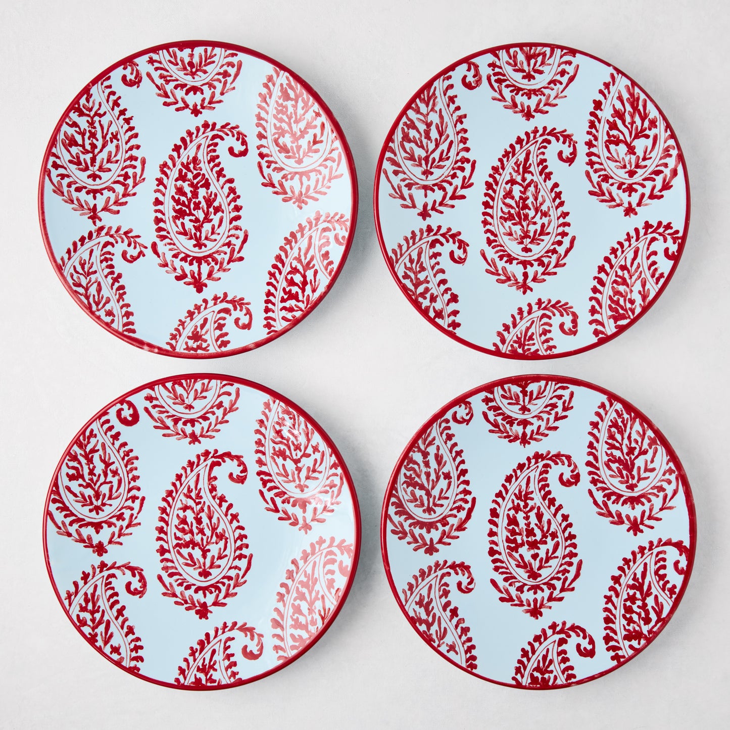Four Peter Dunham + Hudson Grace Red Kashmir hand-painted paisley salad plates with light blue background.