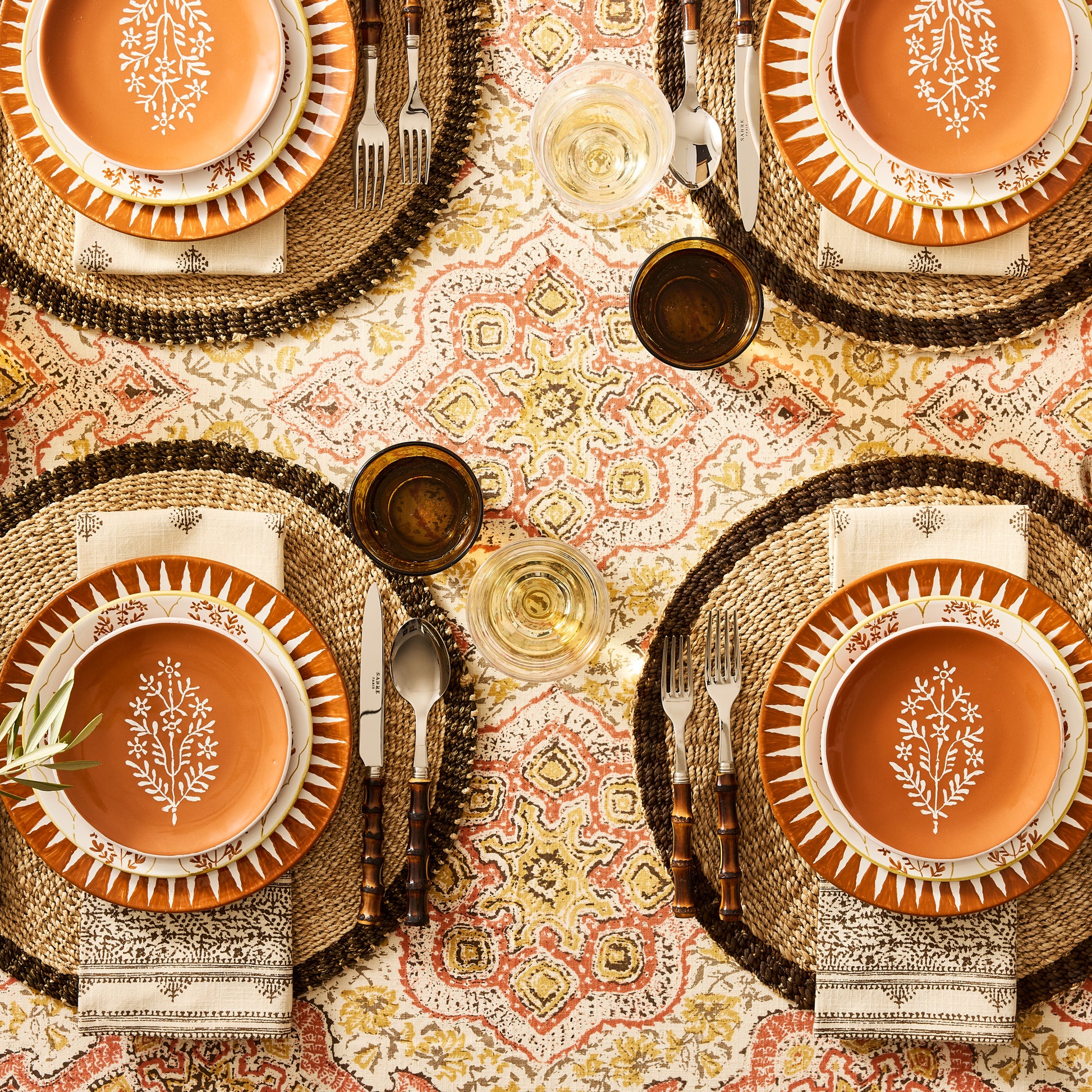Peter Dunham + Hudson Grace Spice Orange Hand-Painted Sunburst Dinner Plate on a patterned tablecloth.