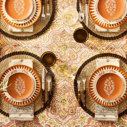Peter Dunham + Hudson Grace Spice Orange Hand-Painted Sunburst Dinner Plate on a patterned tablecloth.