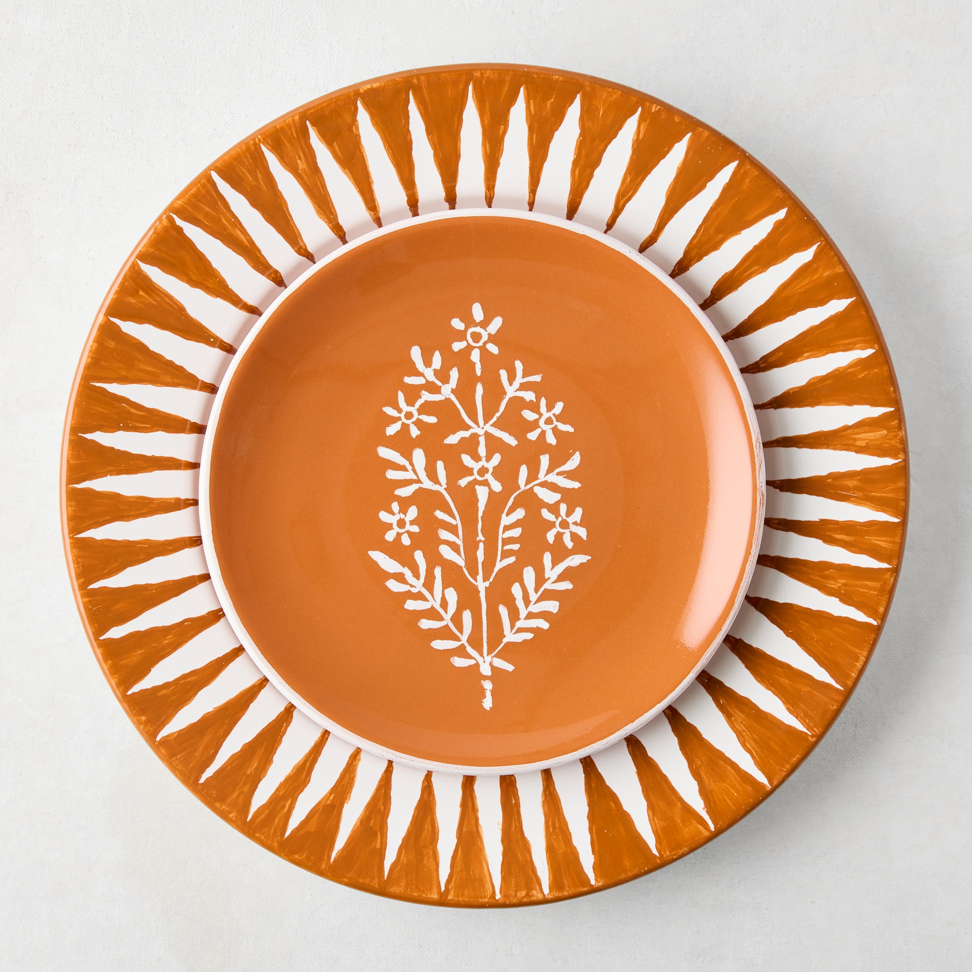 Peter Dunham + Hudson Grace Spice Orange Hand-Painted Sunburst Dinner Plate with a floral design.