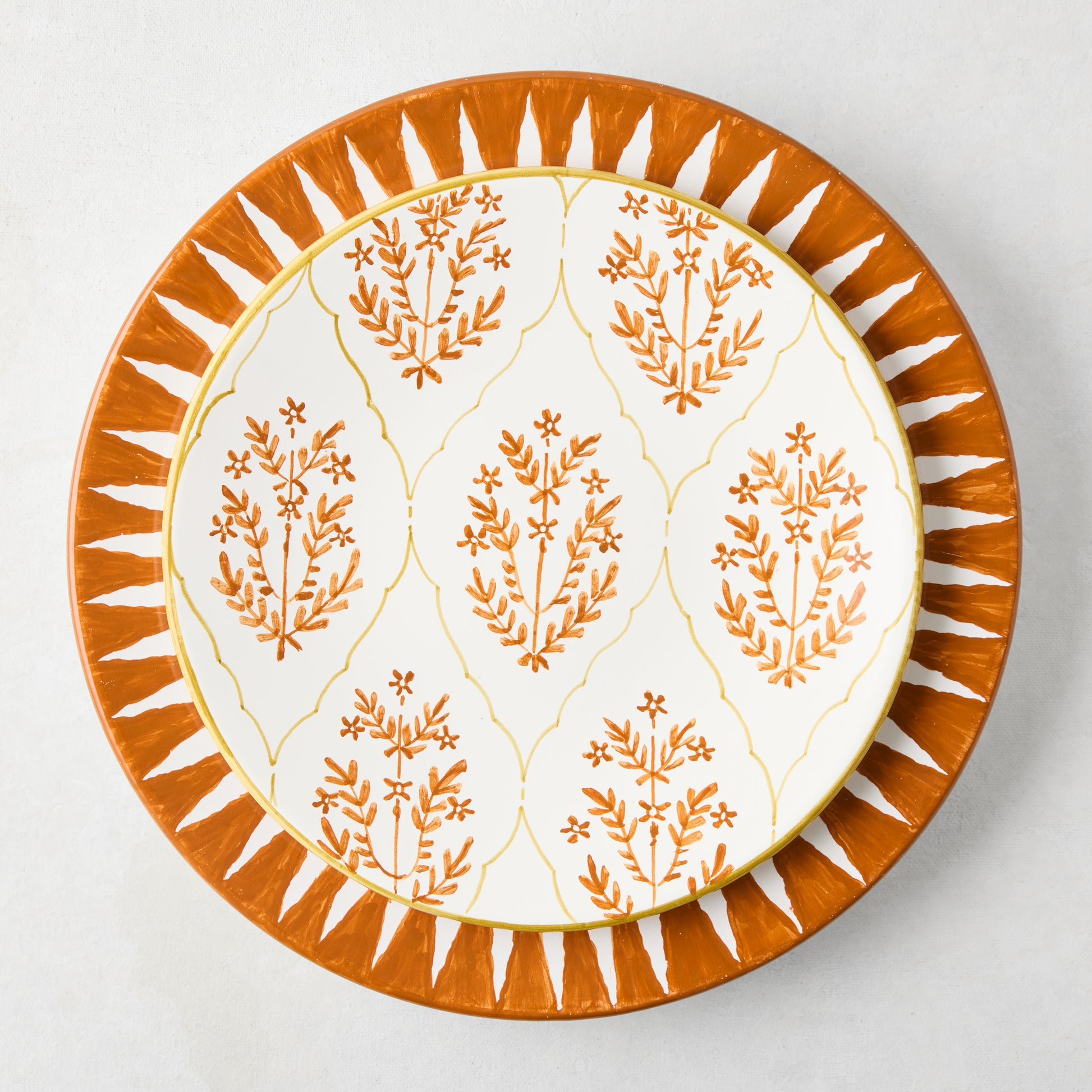 Peter Dunham + Hudson Grace Spice Orange Hand-Painted Sunburst Dinner Plate with a smaller floral patterned plate.