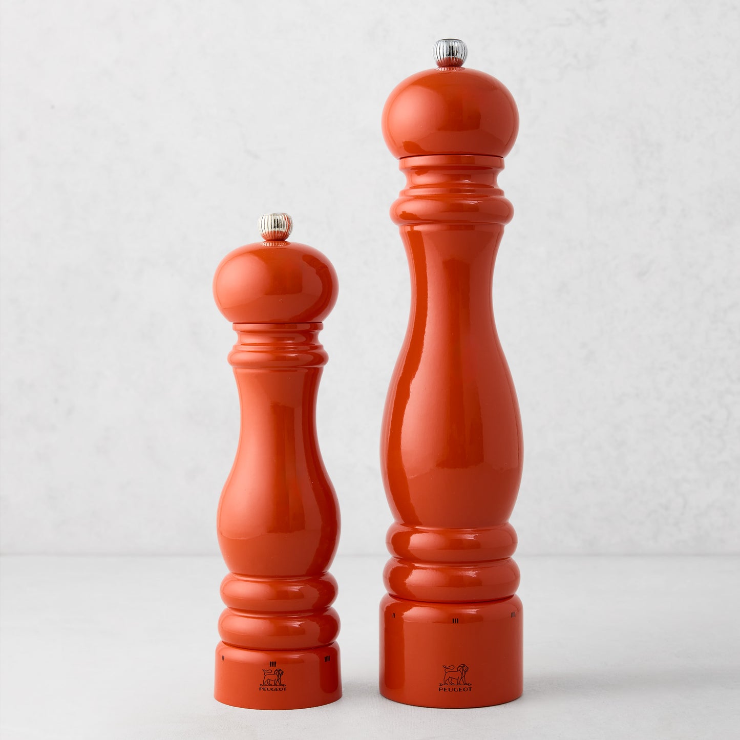 Two Peugeot Paris Exclusive "HG International Orange" beechwood pepper mills, 12" and smaller, with silver tops.