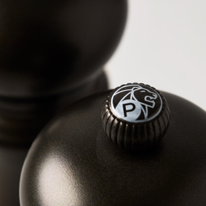 Close-up of a matte black Peugeot Paris pepper mill with a silver "P" and lion logo on top.