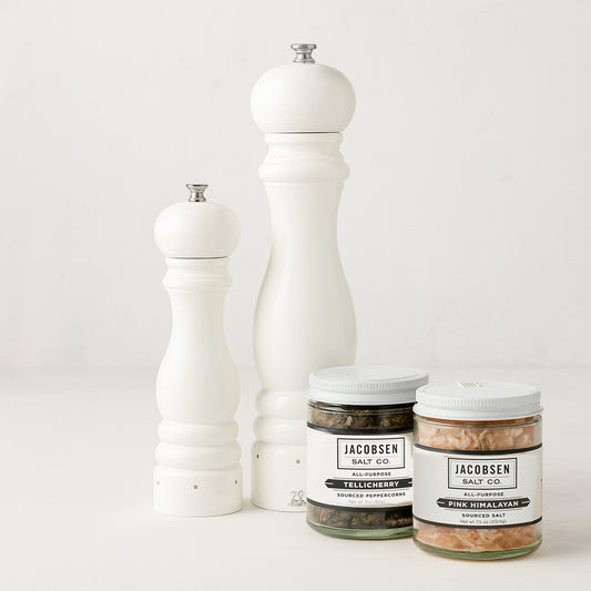Two white lacquer Peugeot mills with Jacobsen Tellicherry peppercorns and pink Himalayan salt jars.
