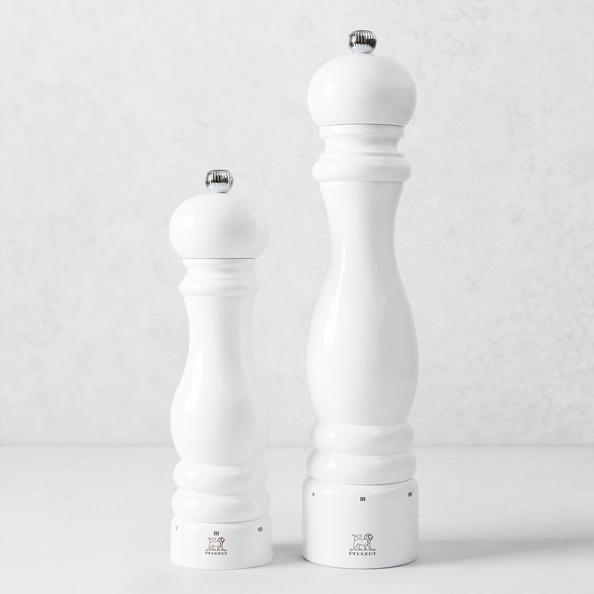 Two Peugeot Paris white lacquer beechwood pepper mills with chrome knobs on a light background.