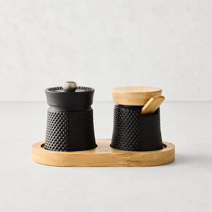 Peugeot Paris black cast iron salt and pepper cellar set with textured finish, bamboo base, lid, and spoon.