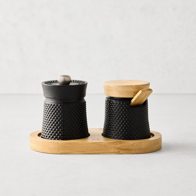 Peugeot Paris black cast iron salt and pepper cellar set with textured finish, bamboo base, lid, and spoon.
