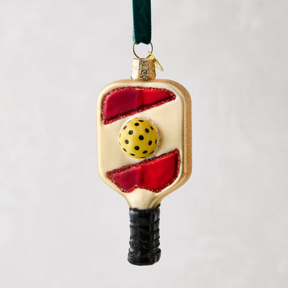 Glittered glass pickleball paddle ornament with red accents, yellow ball, and black handle, hanging from a green ribbon.